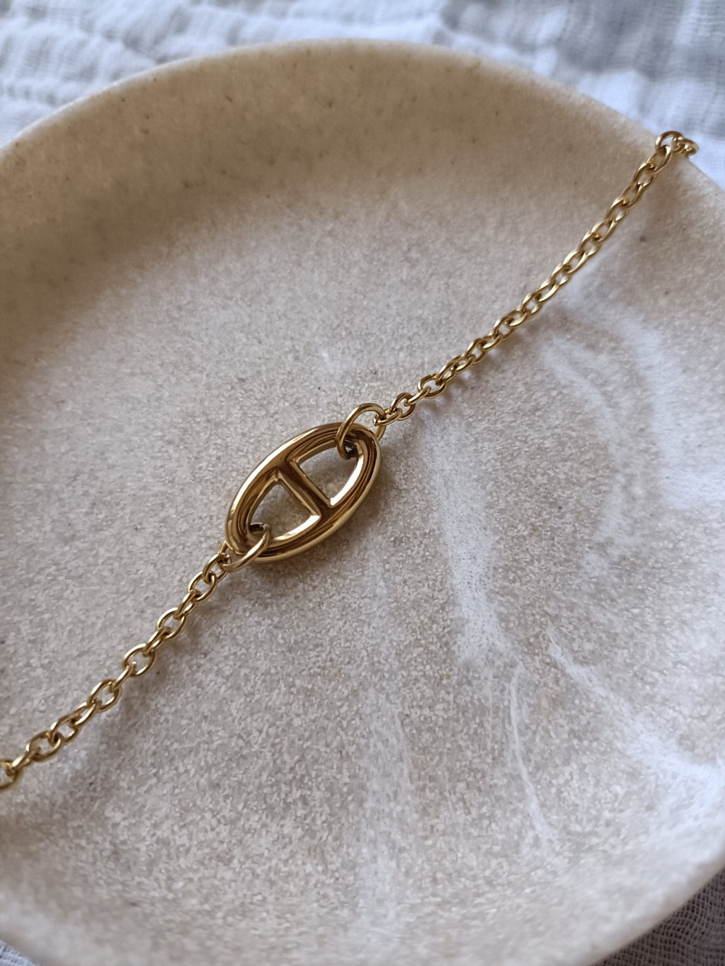 Bracelet grosse maille marine doré en acier inoxydable posé sur une coupelle
