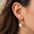 Boucle d'oreille créole dorée en acier inoxydable avec pendentif fleur effet nacré portée sur une oreille