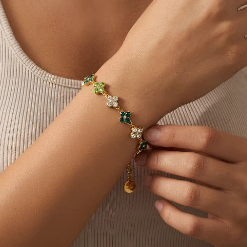 bracelet à trefles verts foncé, vert pomme et blanc strass sur chaine dorée en acier inoxydable porté au poignet d'une femme