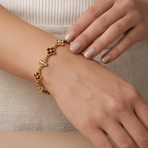 bracelet à trefles marron foncé, marron glacé et blanc  strass sur chaine dorée en acier inoxydable porté au poignet d'une femme