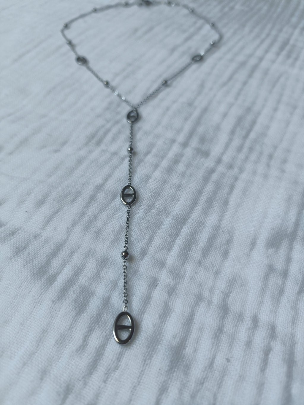Gros plan sur un collier Y argenté en acier inoxydable avec mailles marines et perles