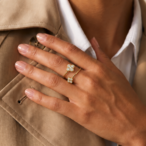 Bague dorée en acier inoxydable avec trèfles croisés et pierres synthétiques blanches portée sur doigt d'une main de femme