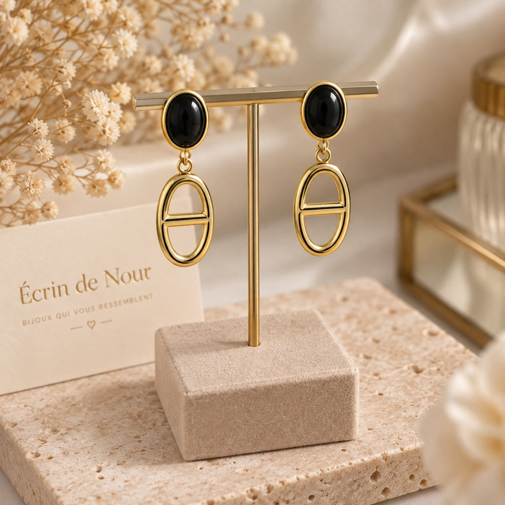Paire de boucles d'oreilles pendantes dorées et noires en acier inoxydable présentée sur un support