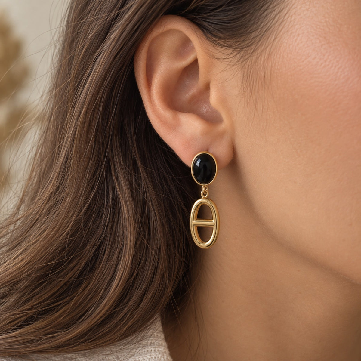 Boucle d'oreille pendante dorée et noire en acier inoxydable portée sur une oreille