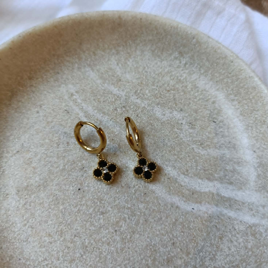 boucles créoles dorées à trefles noir en acier posées sur une coupelle beige