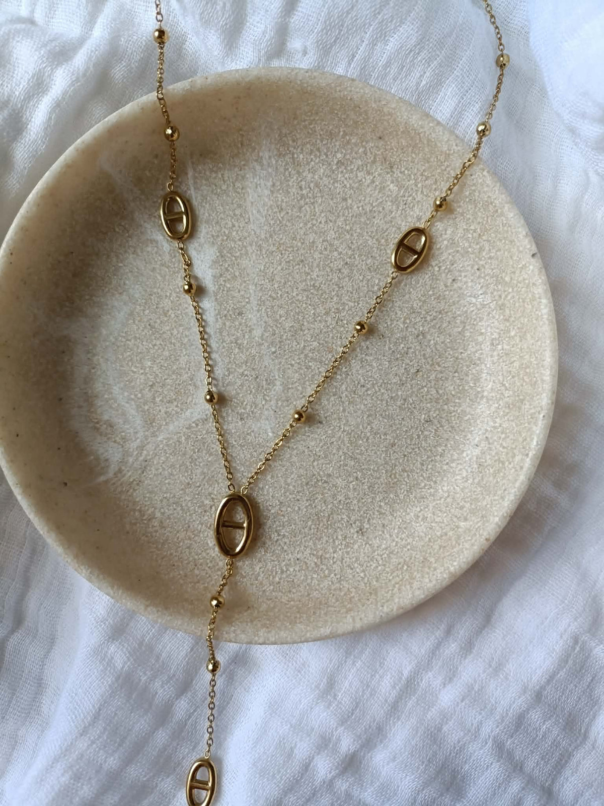 Gros plan sur un collier Y doré en acier inoxydable avec mailles marines et perles
